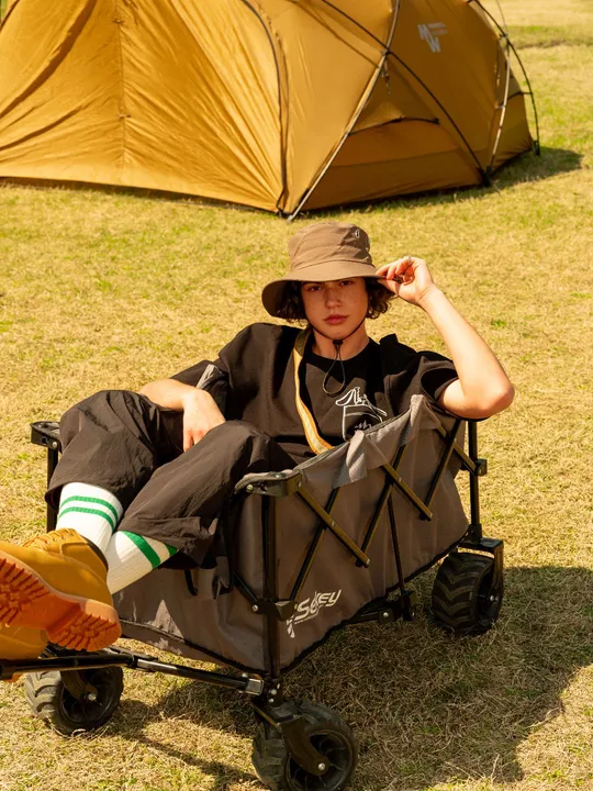 一个戴帽子的年轻人坐在有帐篷背景的小推车上