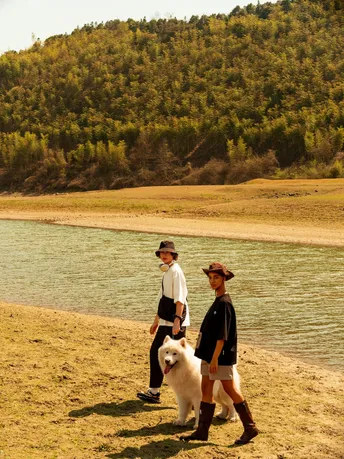 一个男子和一个男孩在河边的海滩上遛一只白色的狗。