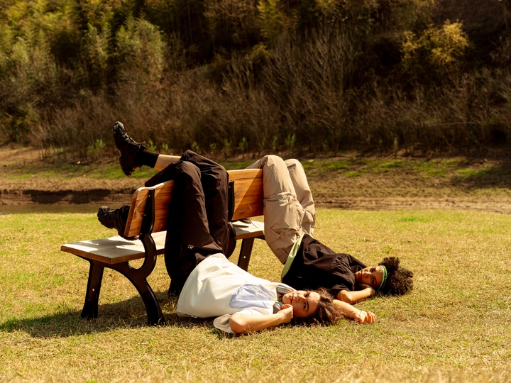 一个男子和一个女人躺在一片草地上的一张木凳上 而另一个人躺在草地上。