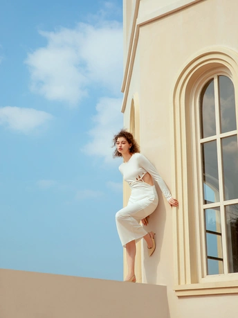 一位穿着白色连衣裙的女人站在建筑物的边缘 倚靠在窗户上