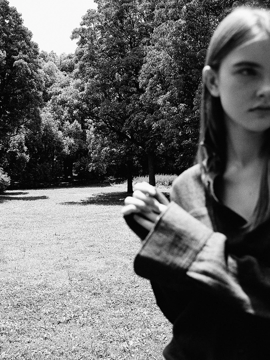 一张黑白照片 一个年轻女孩站在公园里 背景有树木。