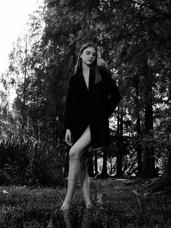 一个穿着黑白连衣裙的年轻女子站在森林中的草地上 周围有树木和一把黑白相间的伞。