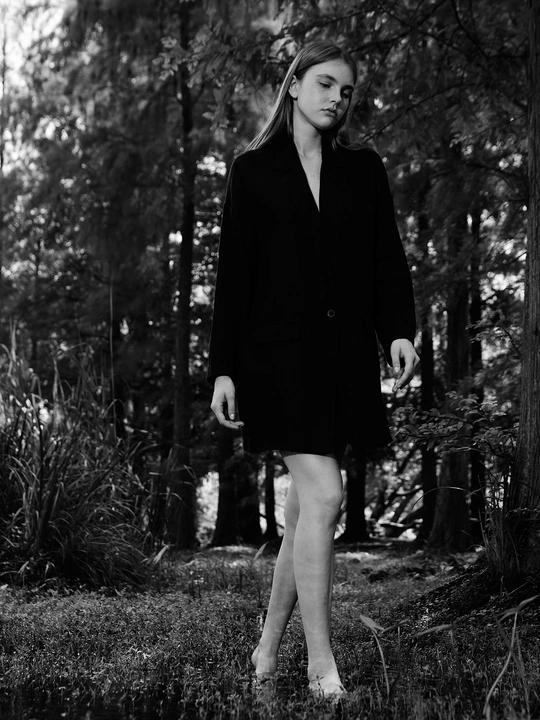 一位穿着黑色连衣裙的女人穿过一棵棵树的森林。