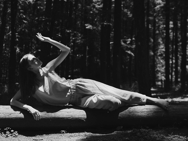 一张黑白照片 一位年轻女子穿着裙子躺在倒下的树上 在森林中。