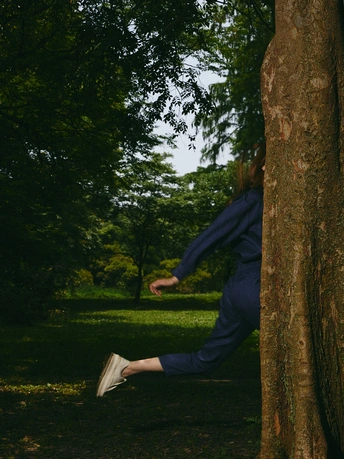 一位年轻男子靠在公园里一棵树旁 女孩跳起来接飞盘。