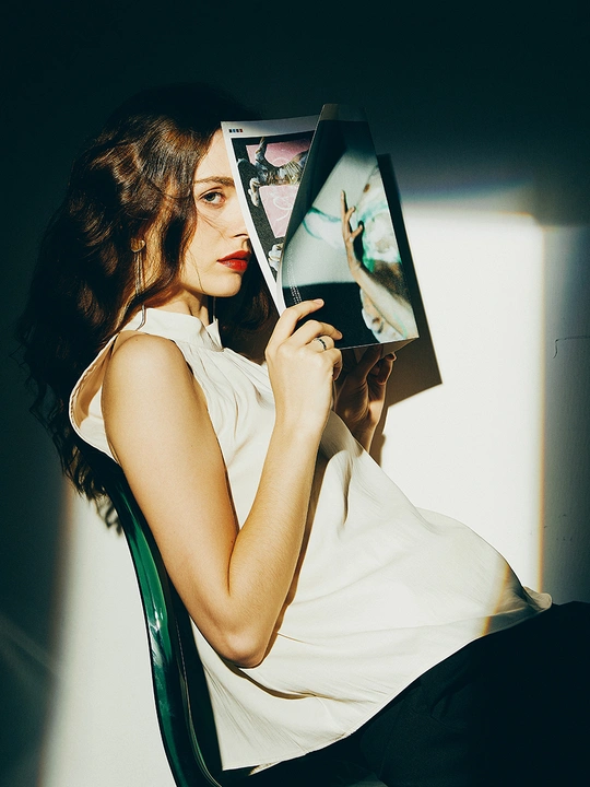 一个年轻女子坐在白色椅子上 举着杂志挡在脸前