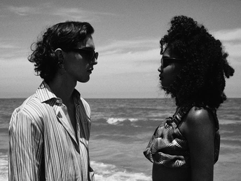 一张黑白照片 一对年轻男女站在海滩上 面向海洋。