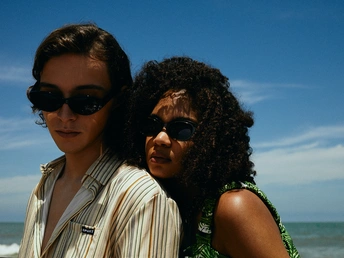 一个年轻男子和一个穿着太阳镜的女人在海滩上 面对着海洋站立。