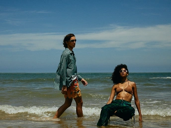 一个男子和一个女子站在海滩上的水中 而另一个男子在海洋中玩耍。