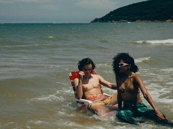 一个年轻男子和女子坐在海滩上的水中 一个女孩也坐在水中。