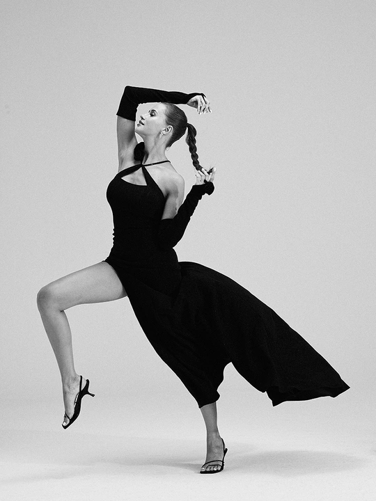 一张黑白照片 一位穿着黑色连衣裙的女人在空中舞动她的腿。