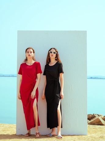 戴太阳镜和连衣裙的女人倚靠在白色墙壁上 位于水体附近的沙滩上。