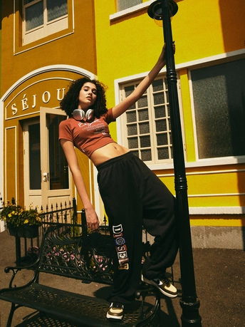 一位年轻女子站在一栋建筑前 靠在一盏路灯柱上 坐在长凳上。