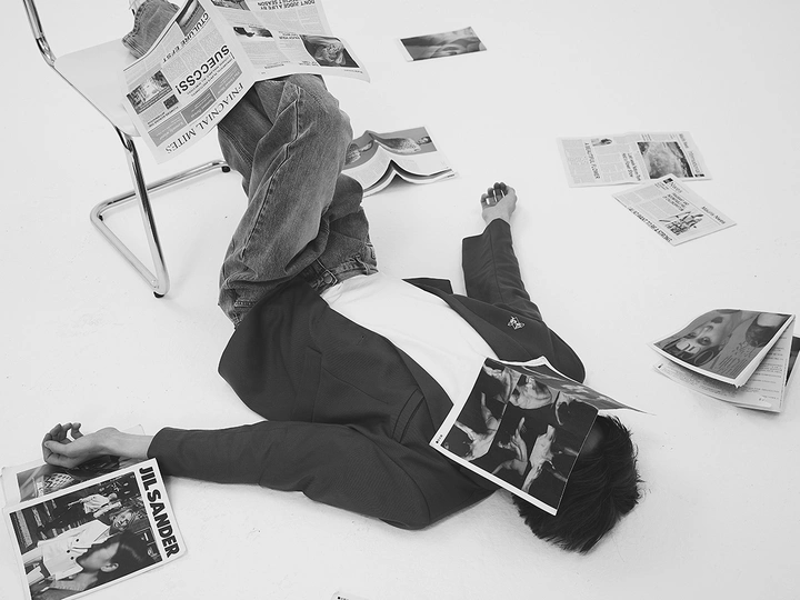一个年轻人躺在椅子上 周围堆满了报纸和杂志。