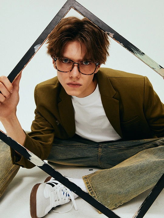 一个戴眼镜、夹克和西装的年轻人坐在地板上