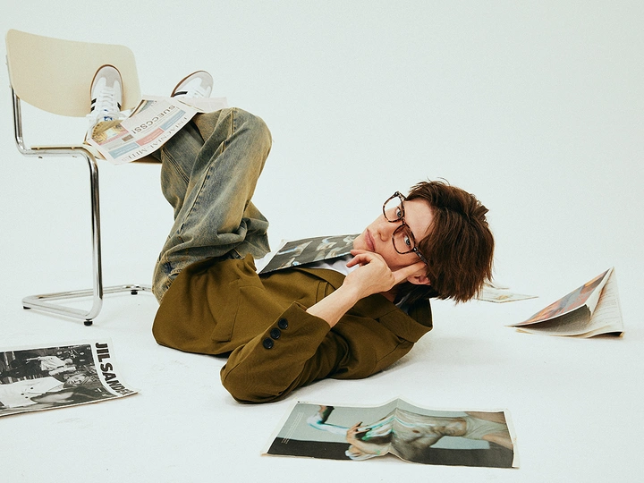 一个戴眼镜的年轻男子躺在地上 面前有一把椅子和一本杂志。