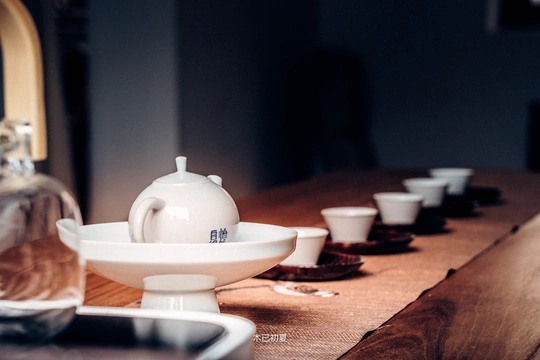 一张长桌子 上面有白色的杯子、茶托和一只茶壶。