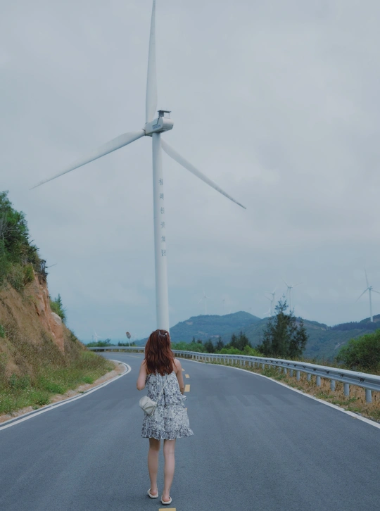 一位穿着连衣裙的年轻女子走在有风车作背景的路上