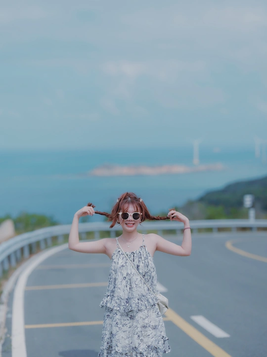 一个戴太阳镜的年轻女子站在高速公路上 双手向前伸展 面对海洋。