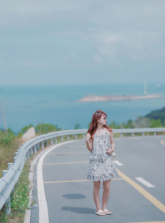 沿着海边的公路 一个穿着连衣裙的年轻女子正在行走。