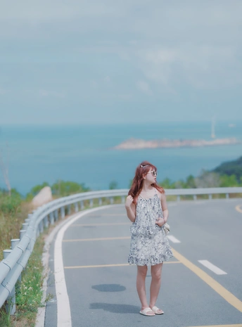 沿着海边的公路 一个穿着连衣裙的年轻女子正在行走。