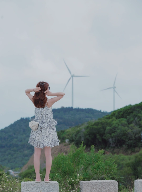 站在山丘上的穿着连衣裙的年轻女子正在观看风车。