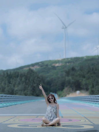 一个年轻女孩坐在桥上 背景中有风车和风力发电机。