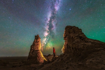 一个站在岩石上仰望天空中的星星的男人