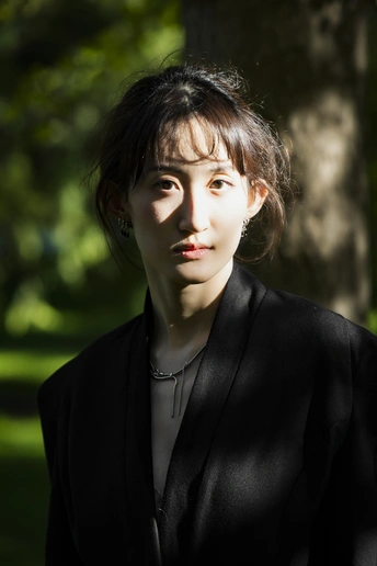 一位穿着全黑衣服的年轻女子在公园里为肖像摆姿势 背景中有树木。