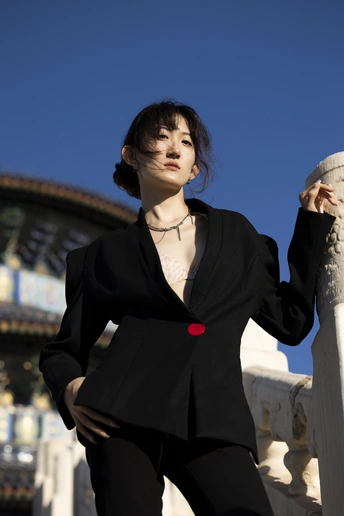 一位穿着黑色西装的年轻女子 倚靠在建筑物前的围栏上。