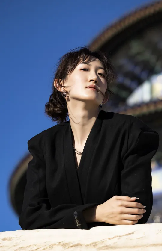 一位穿着全黑衣服的年轻女子站在一栋建筑前 太阳在天空中高高升起。