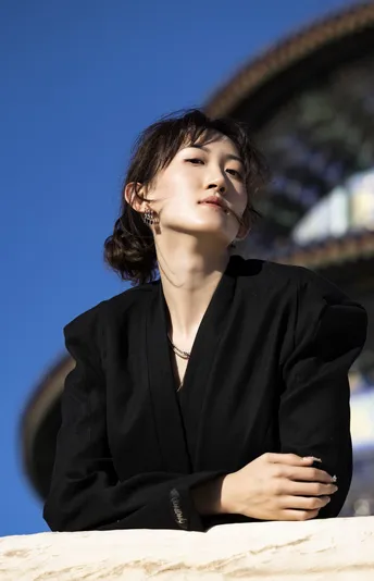 一位穿着全黑衣服的年轻女子站在一栋建筑前 太阳在天空中高高升起。