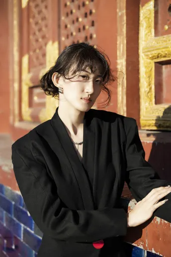 一位穿着全黑衣服的年轻女子站在一座寺庙的墙前