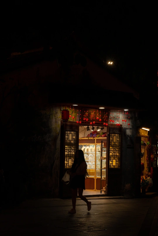 夜晚的黑暗街道 一个人在照亮了商店或餐厅的人行道上行走。