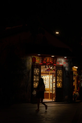 夜晚的黑暗街道 一个人在照亮了商店或餐厅的人行道上行走。