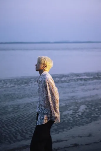 一位妇女在沙滩上行走 凝视着海洋 远处站着一个男人。