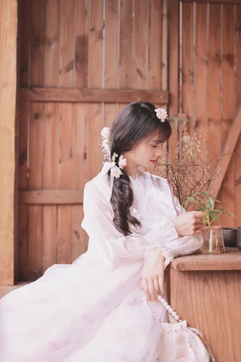 一个穿着传统服装的年轻女子坐在木结构建筑外面 手里拿着一束花。