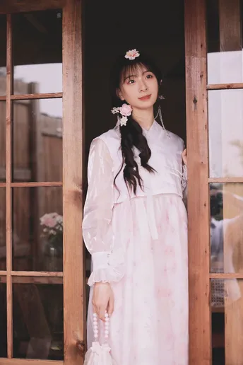 一位穿着白色连衣裙上粉色花朵的年轻女子站在窗户前