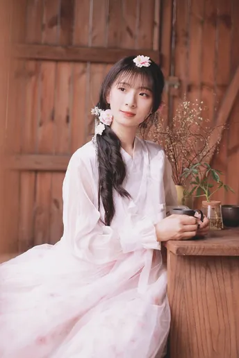 一个穿着传统服装的年轻女子坐在木制桌子旁 头戴鲜花。