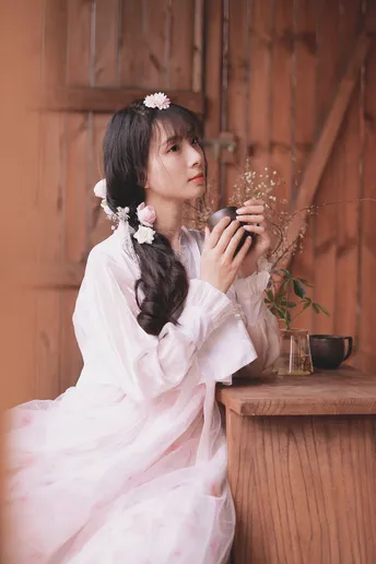 一个穿着白色连衣裙 头戴鲜花的年轻女子坐在木屋外面