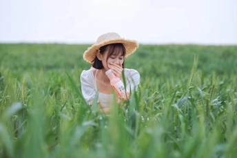 一个戴草帽的年轻女子坐在绿草地上 并伸出她的手向旁边伸展。
