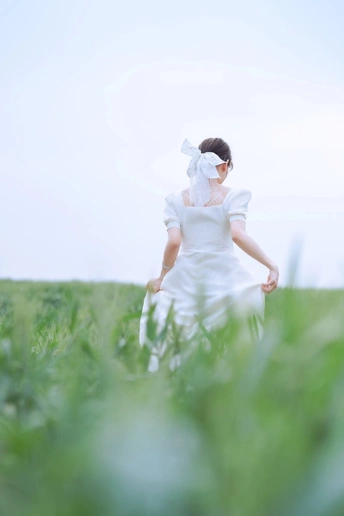 一位穿着白色婚纱和头纱的新娘穿越一片绿色的草地。