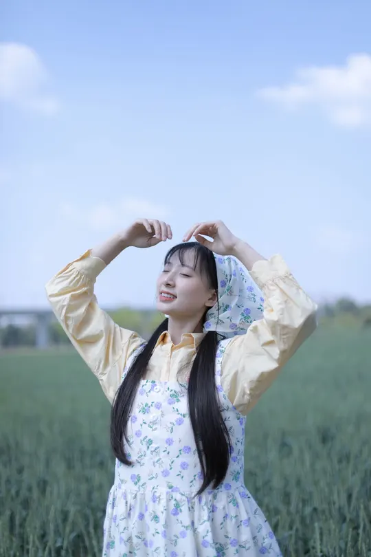 一位穿着连衣裙的年轻女子站在绿地上 双手插在头发里