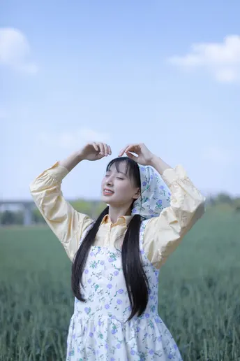 一位穿着连衣裙的年轻女子站在绿地上 双手插在头发里