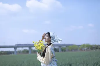 一位穿着连衣裙的年轻女子手持黄色雨伞站在田野中