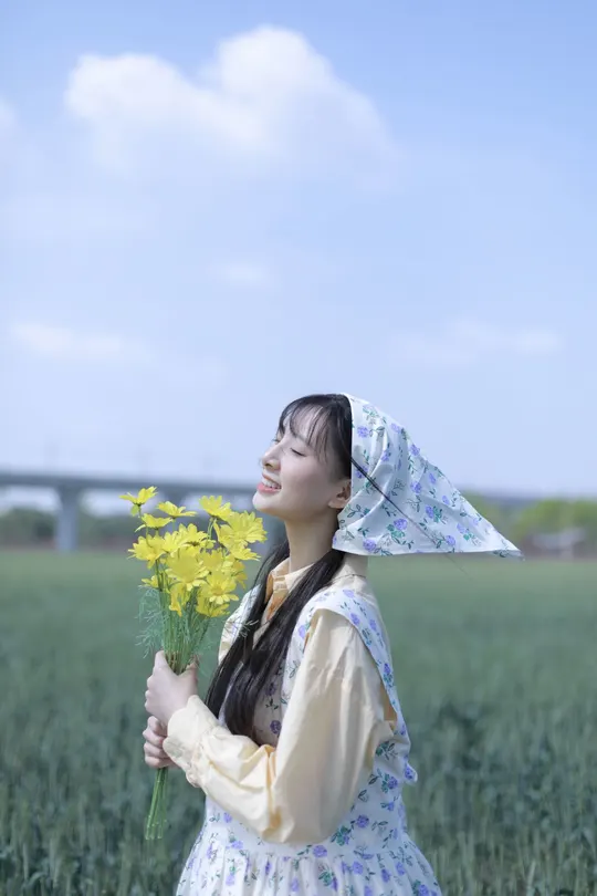 一位穿着连衣裙的年轻女子在田野中拿着黄色花朵。