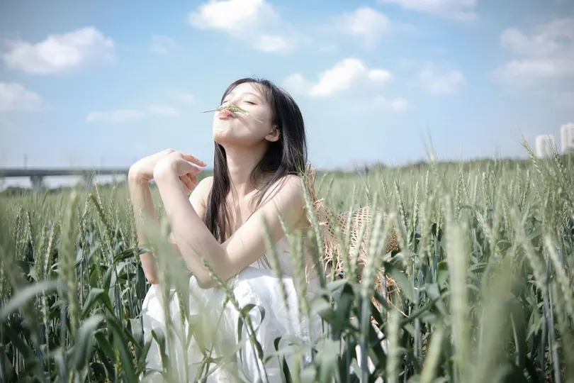 一个穿着白色连衣裙的年轻女子站在一片麦田中。