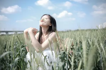 一个穿着白色连衣裙的年轻女子站在一片麦田中。