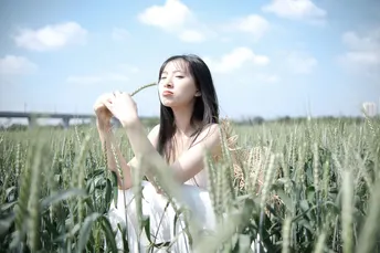 一个穿着白色连衣裙的年轻女子站在一片绿色的麦田中