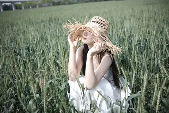 一个穿着连衣裙和草帽的年轻女子坐在一片碧绿的草地上 在一个美丽的麦田里。